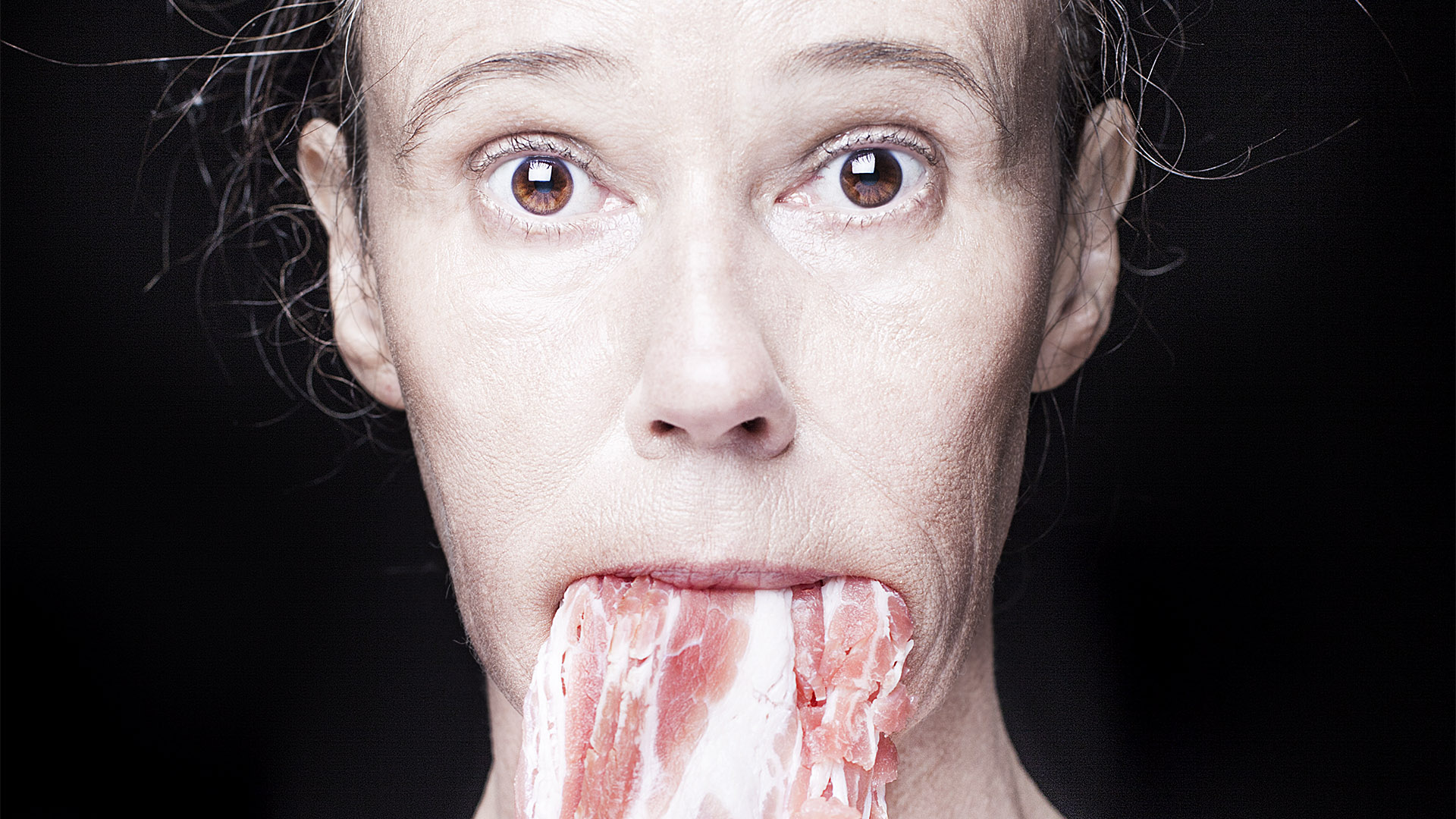 Klickbar bild Det normala livet. Närbild på en kvinna med råa bacon hängande ut ur munnen.