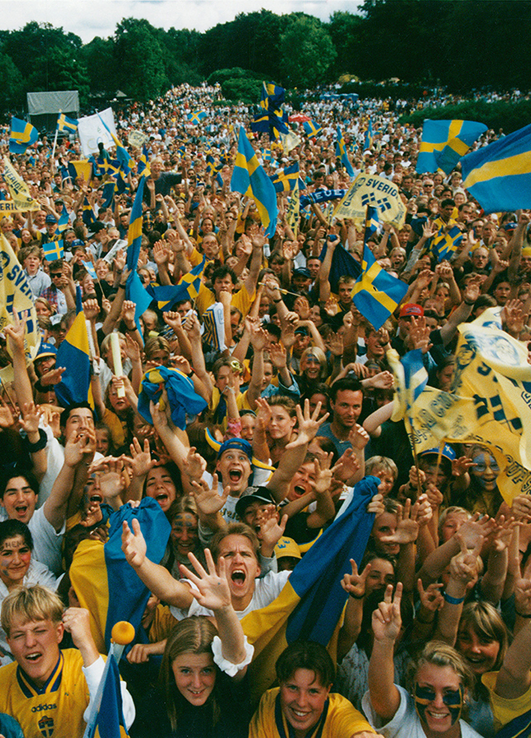 En glad folkmassa som sträcker sig mot kameran i ett jubel. I folkhavet syns många svenska flaggor.