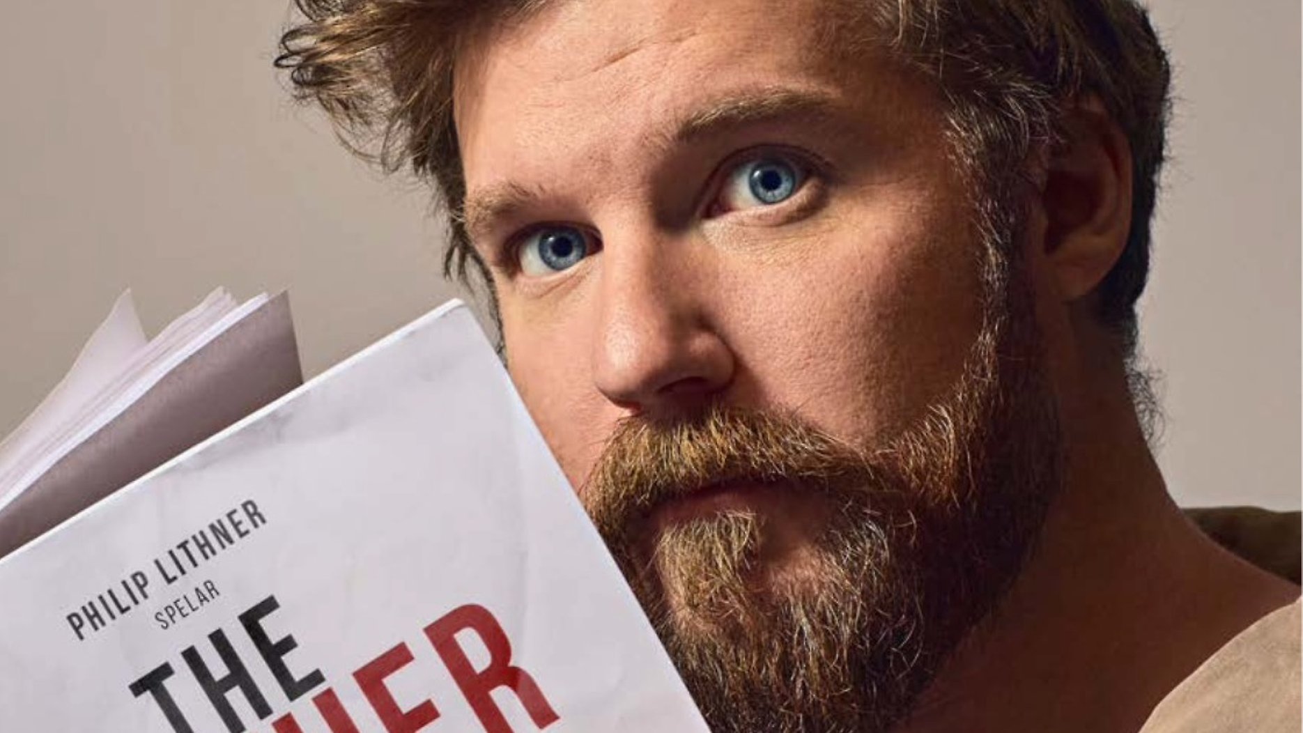 Närbild av ett ansikte på en person som håller upp en bok med texten “Philip Lithner spelar The Father”.